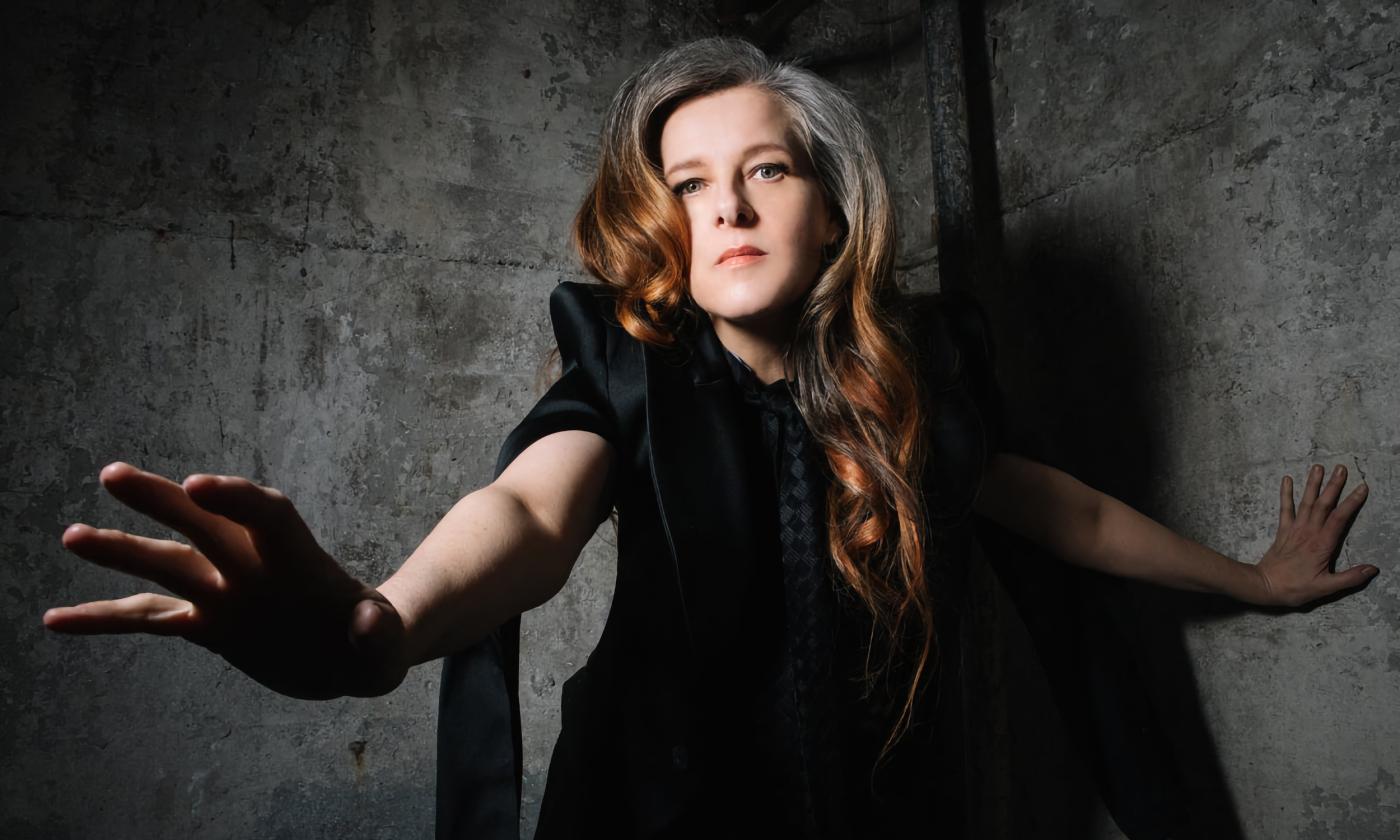 Musical artist, Neko Case, against a grey background, and wearing a black dress