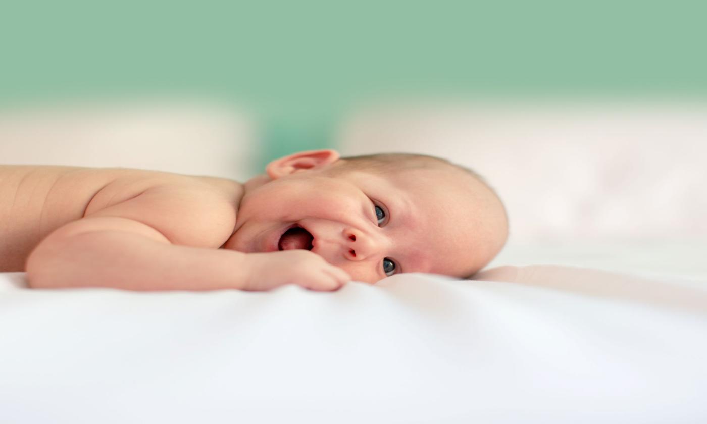 A newborn smiles on a blanket. 