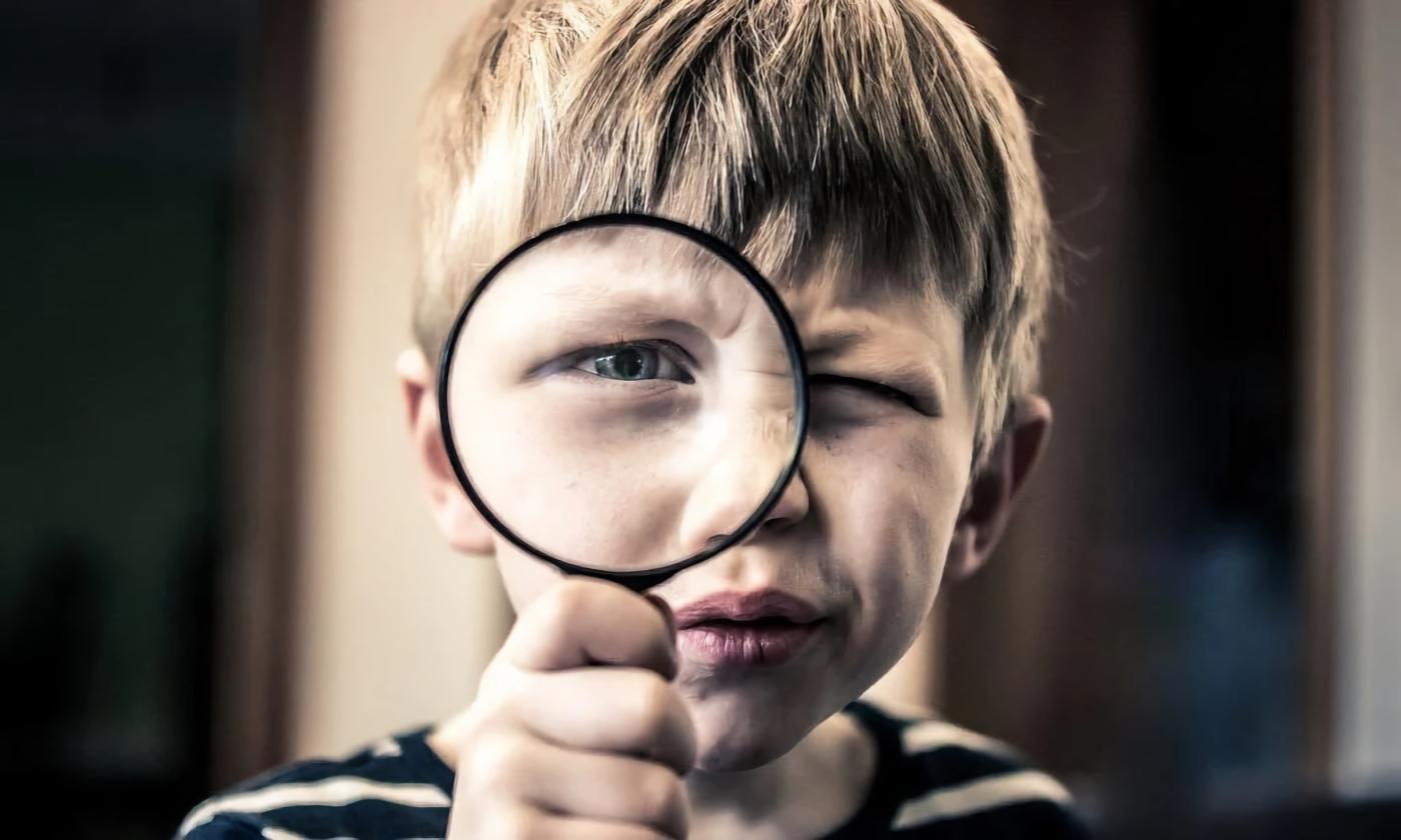 A black and white photo of a young boy looking through a magnifying glass