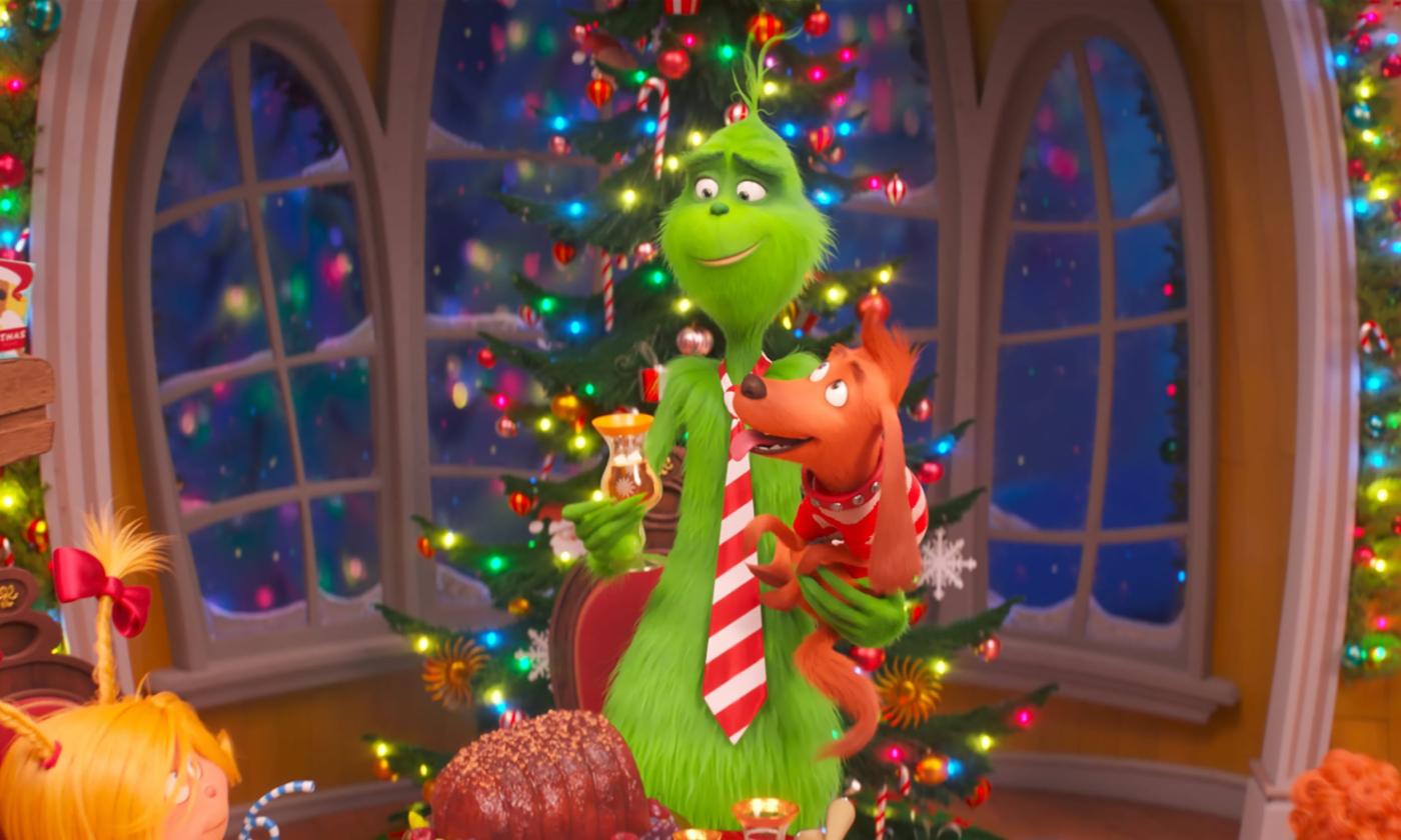 The Grinch in front of a Christmas tree and holding his puppy while celebrating Christmas. 