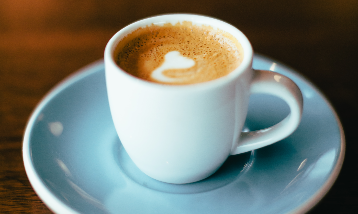 A cup of coffee sits on a blue plate.