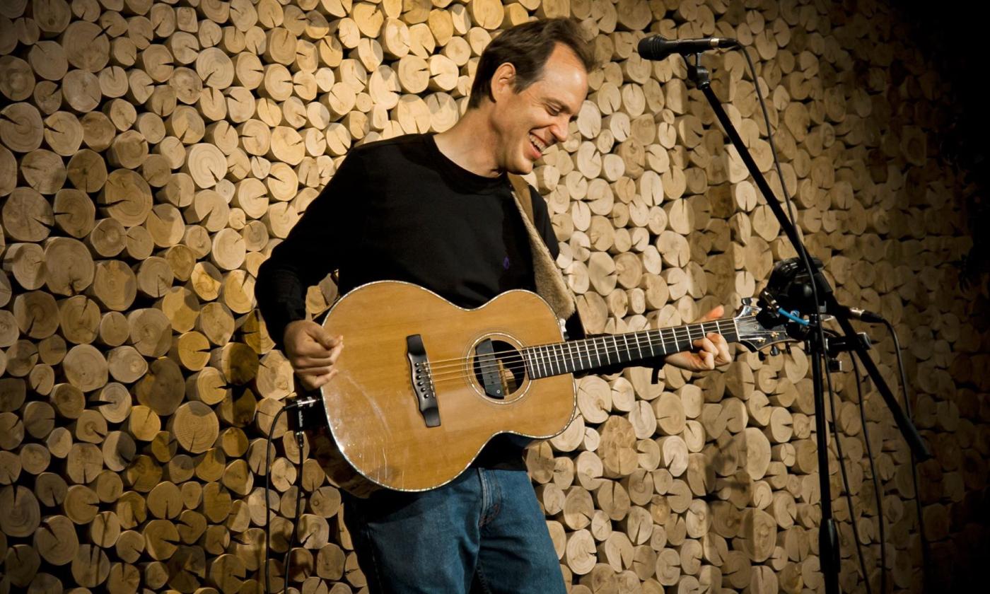 David Wilcox smiles and plays on his guitar. 