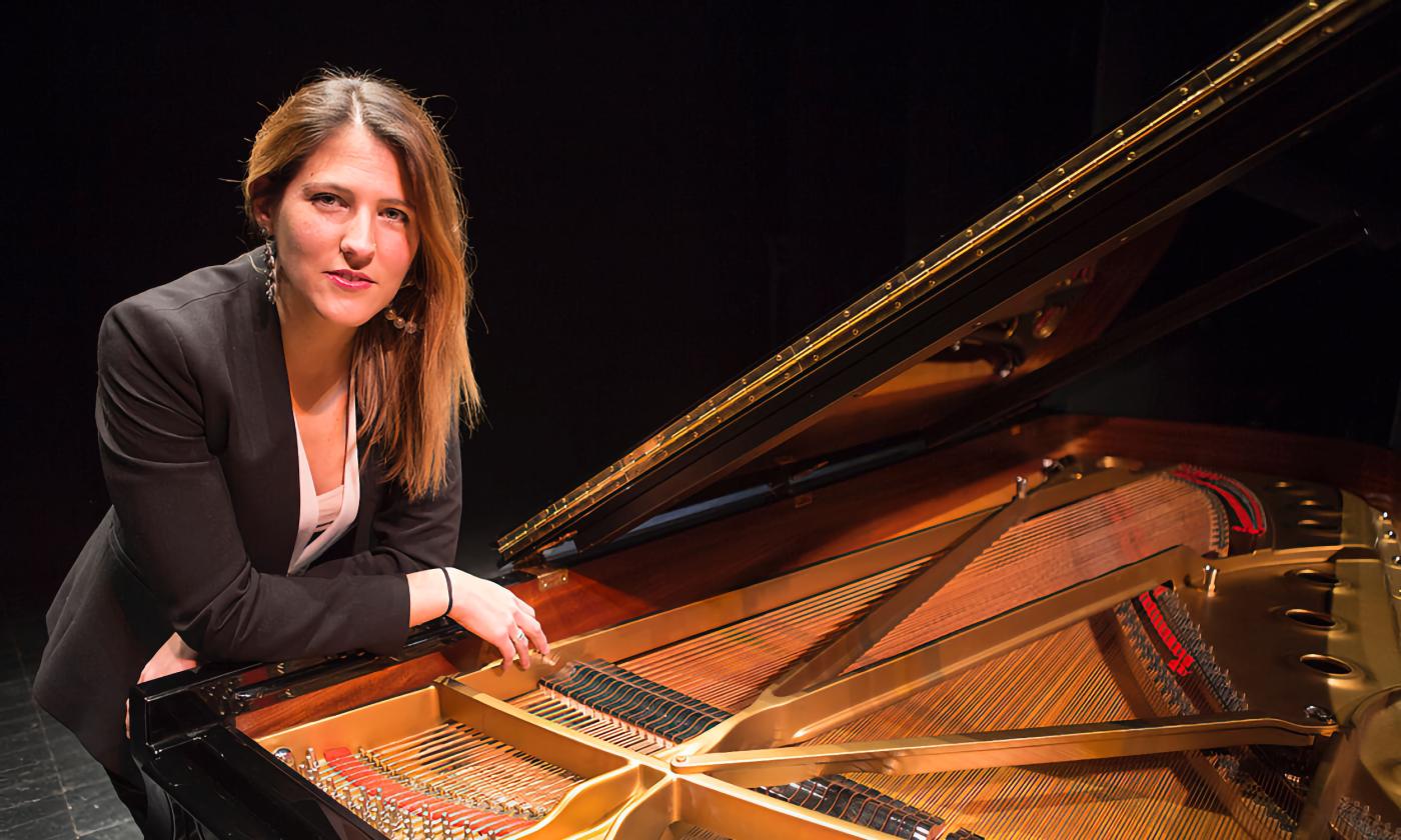 María Delores Gaitán, sitting at an open piano against a black background