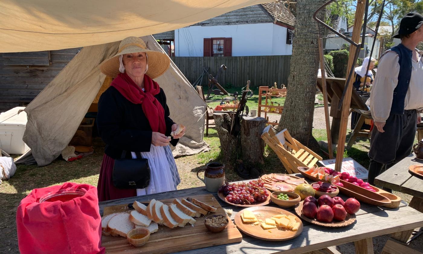 A woman in 16th century garb standing at a table with foods on display