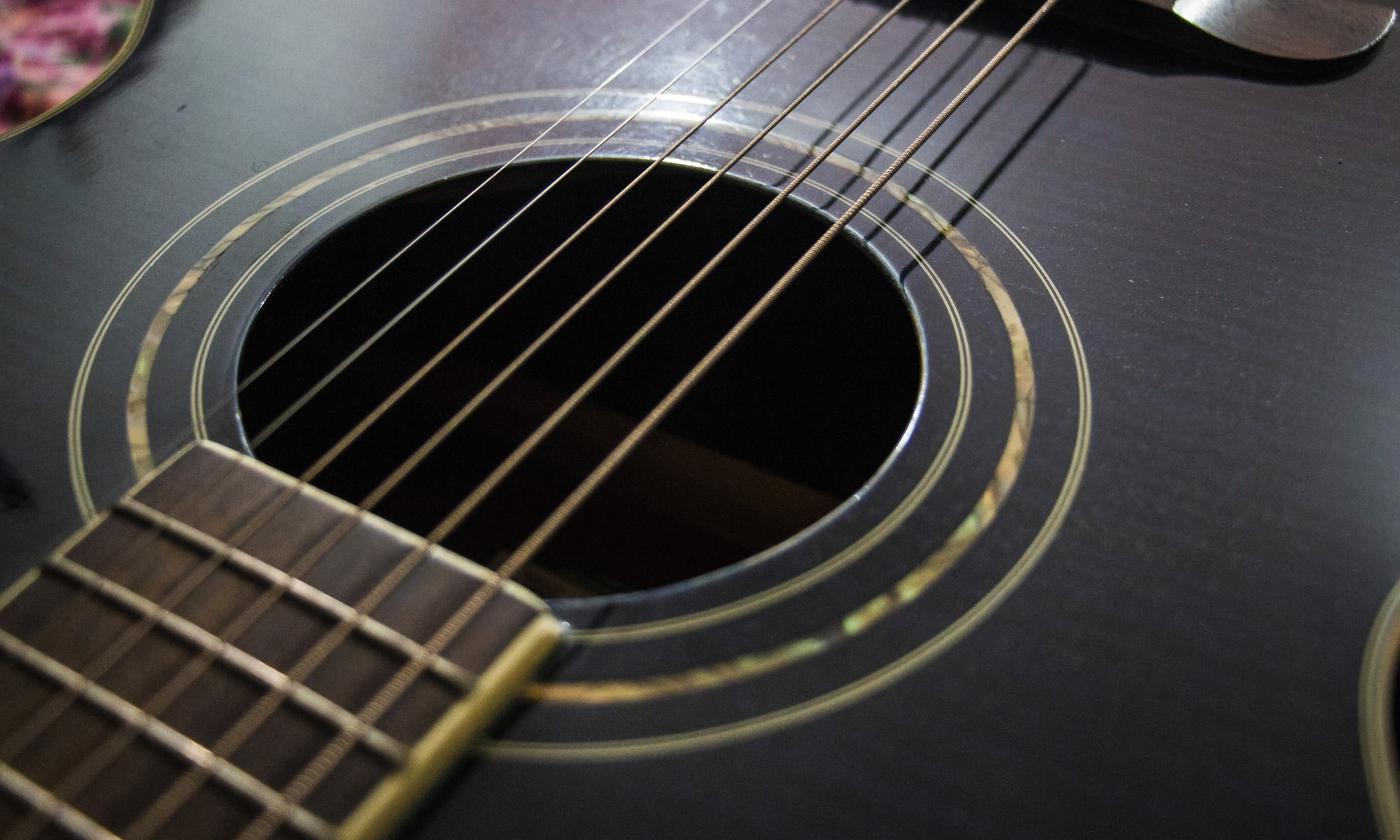 The front of a dark six-string guitar with gold-toned highlights