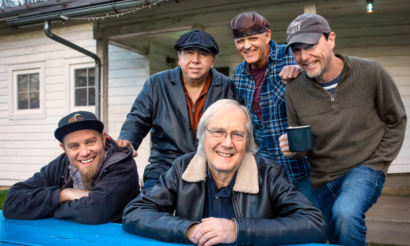 Members of The Weight smile and lean on a table.