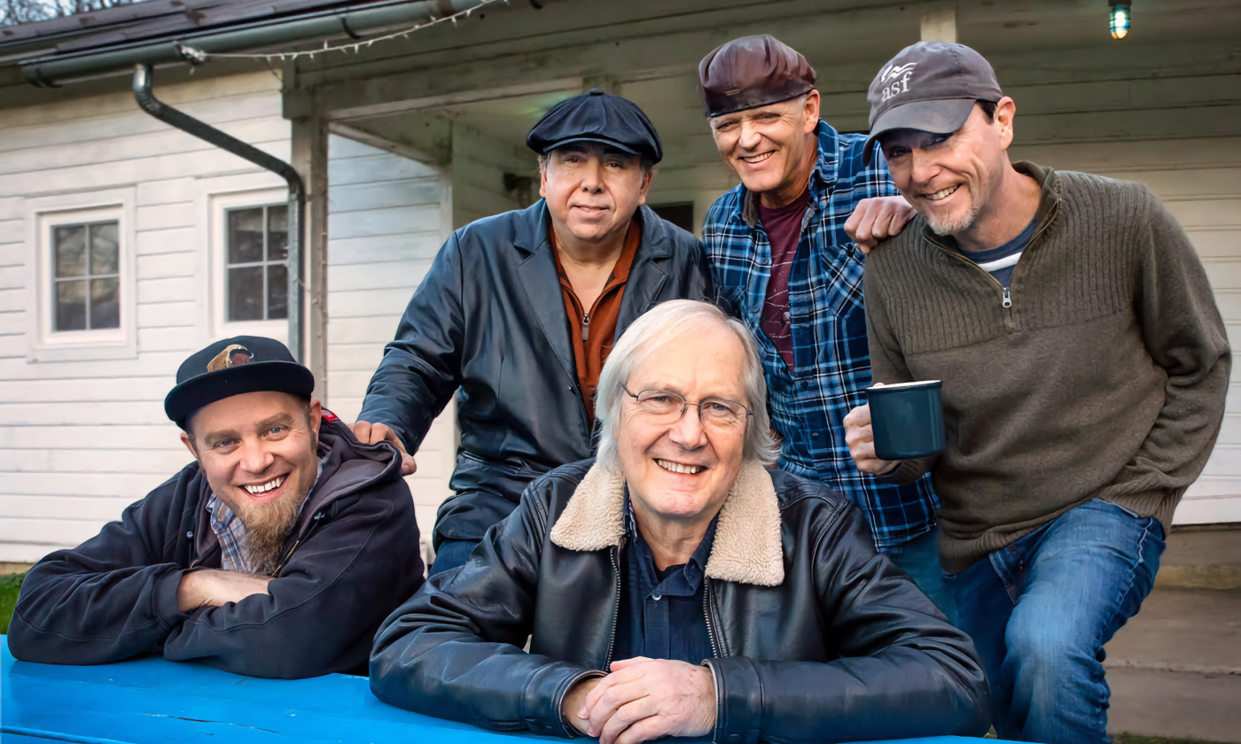 Members of The Weight smile and lean on a table. 