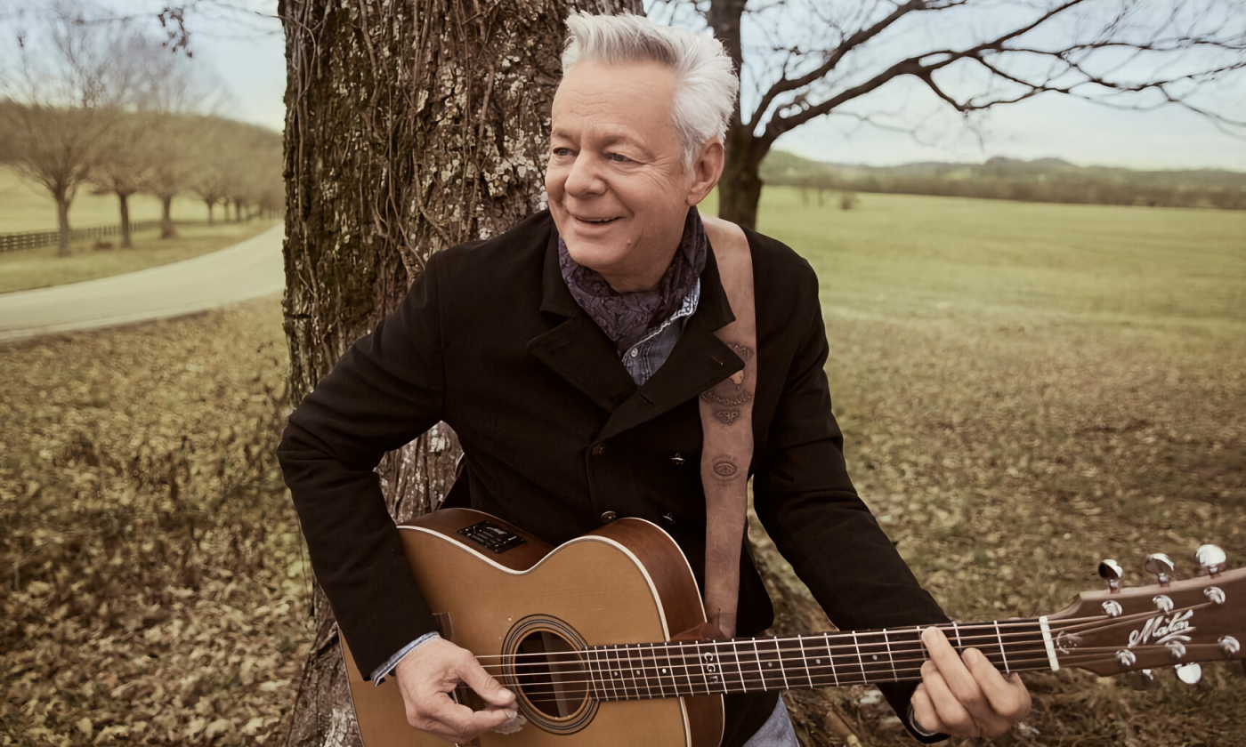 Tommy Emmanuel smiles and strums his guitar. 