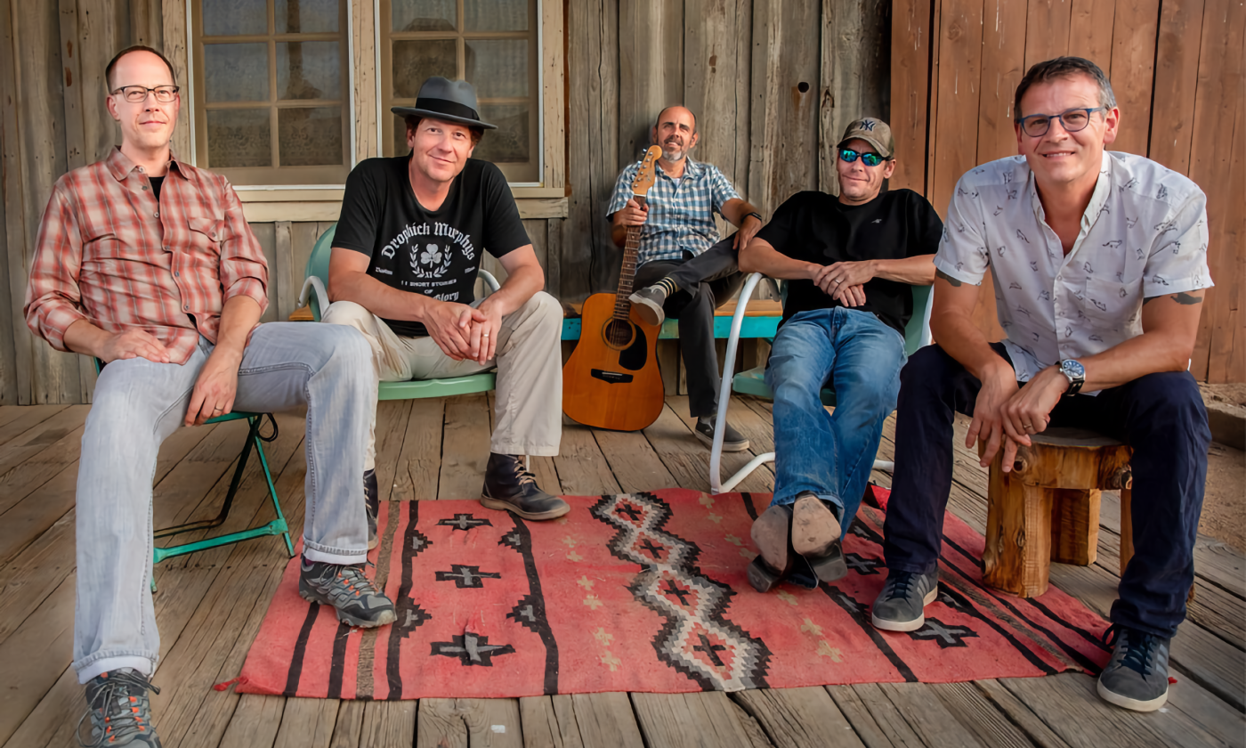 Members of the band smile while sitting on a porch. 