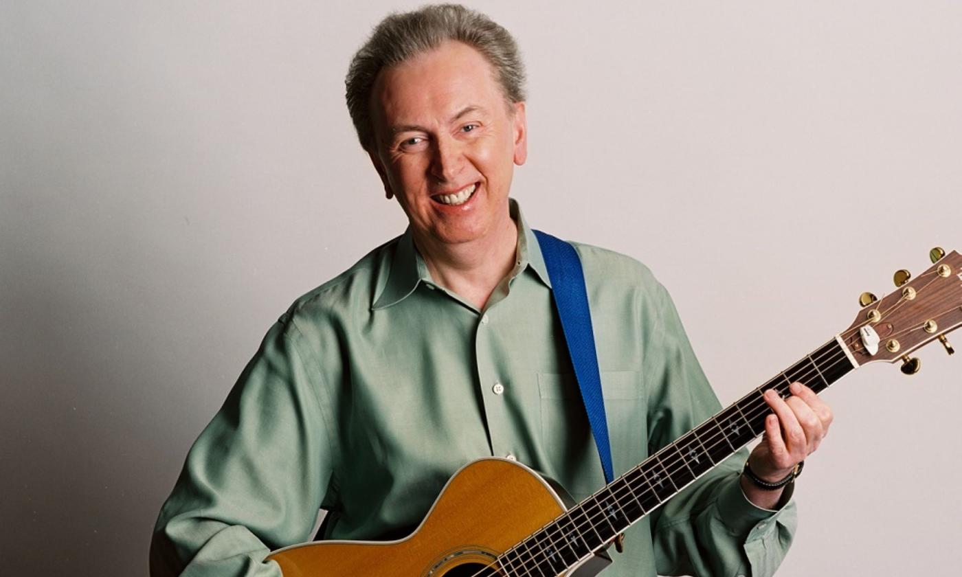 Al Stewart smiles and poses with his guitar.