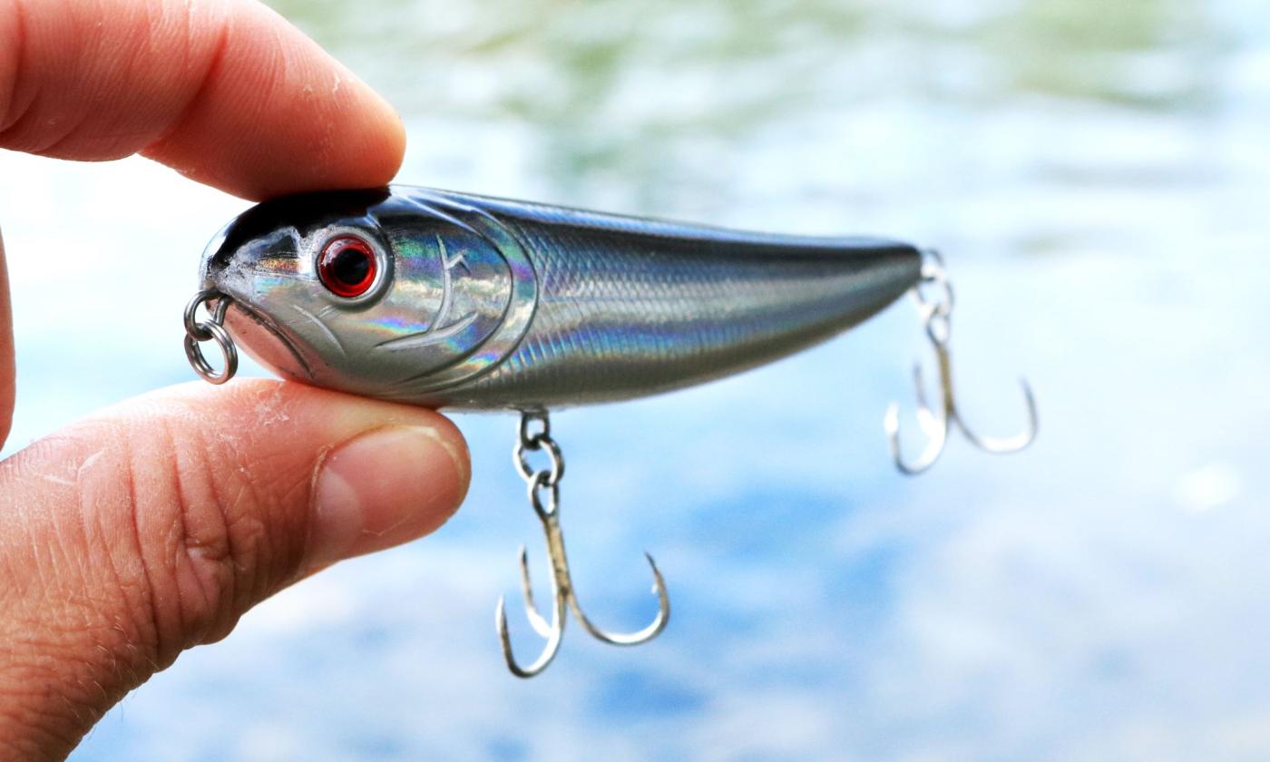 A man holds a fishing hook that is shaped like a fish.