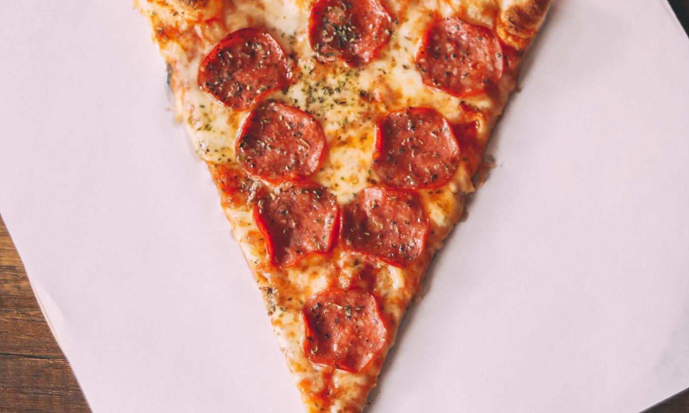A slice of pizza is positioned on parchment paper. 