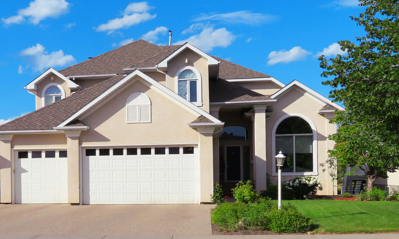 A full color image of a house in the suburbs. It is beige and has a manicured lawn.