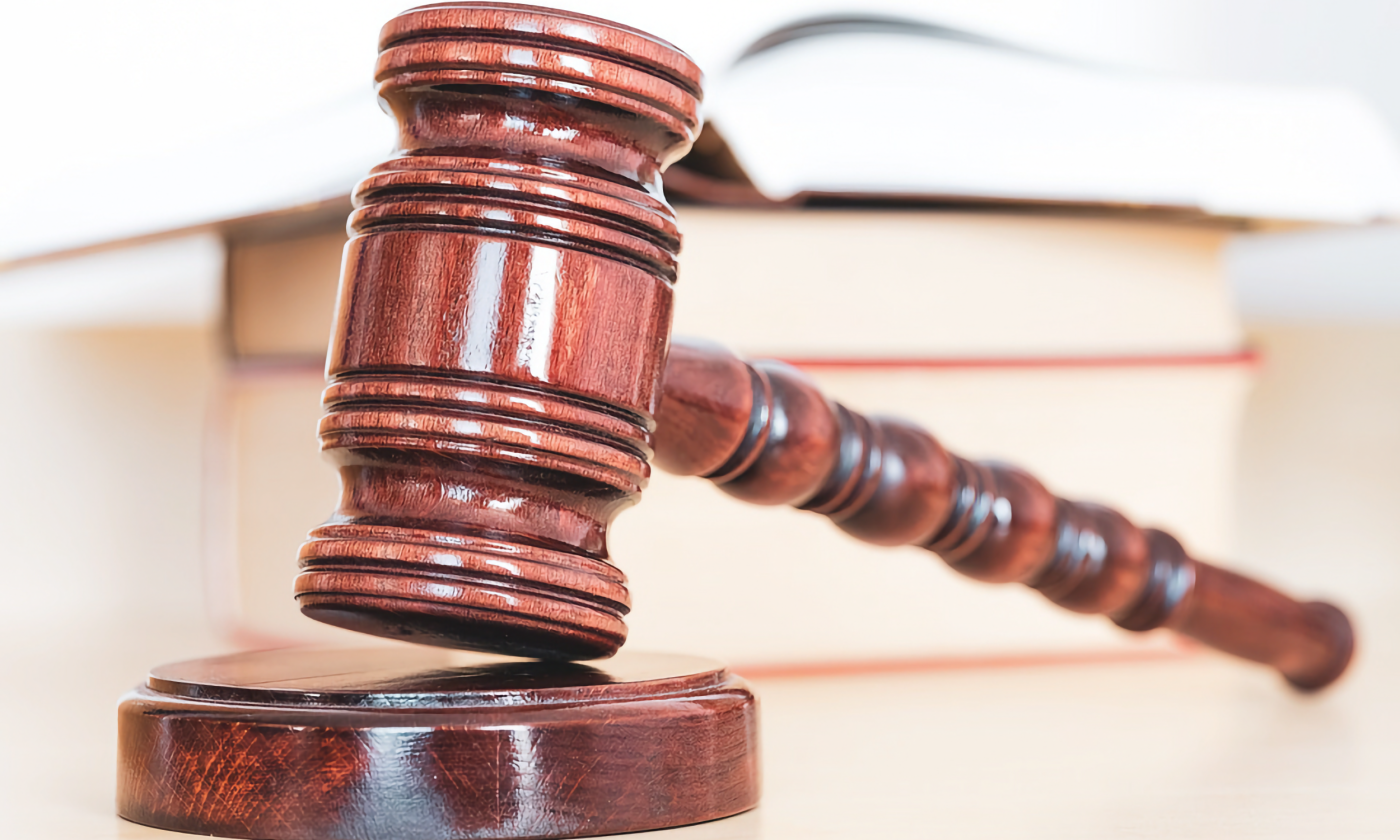 A full color image of a wooden gavel on its stand. Books in the background for academic vibes.