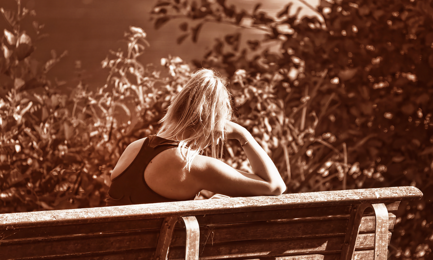 A sepia-toned image of a woman on a bench from behind. She leans her head on her hand as if in distress.