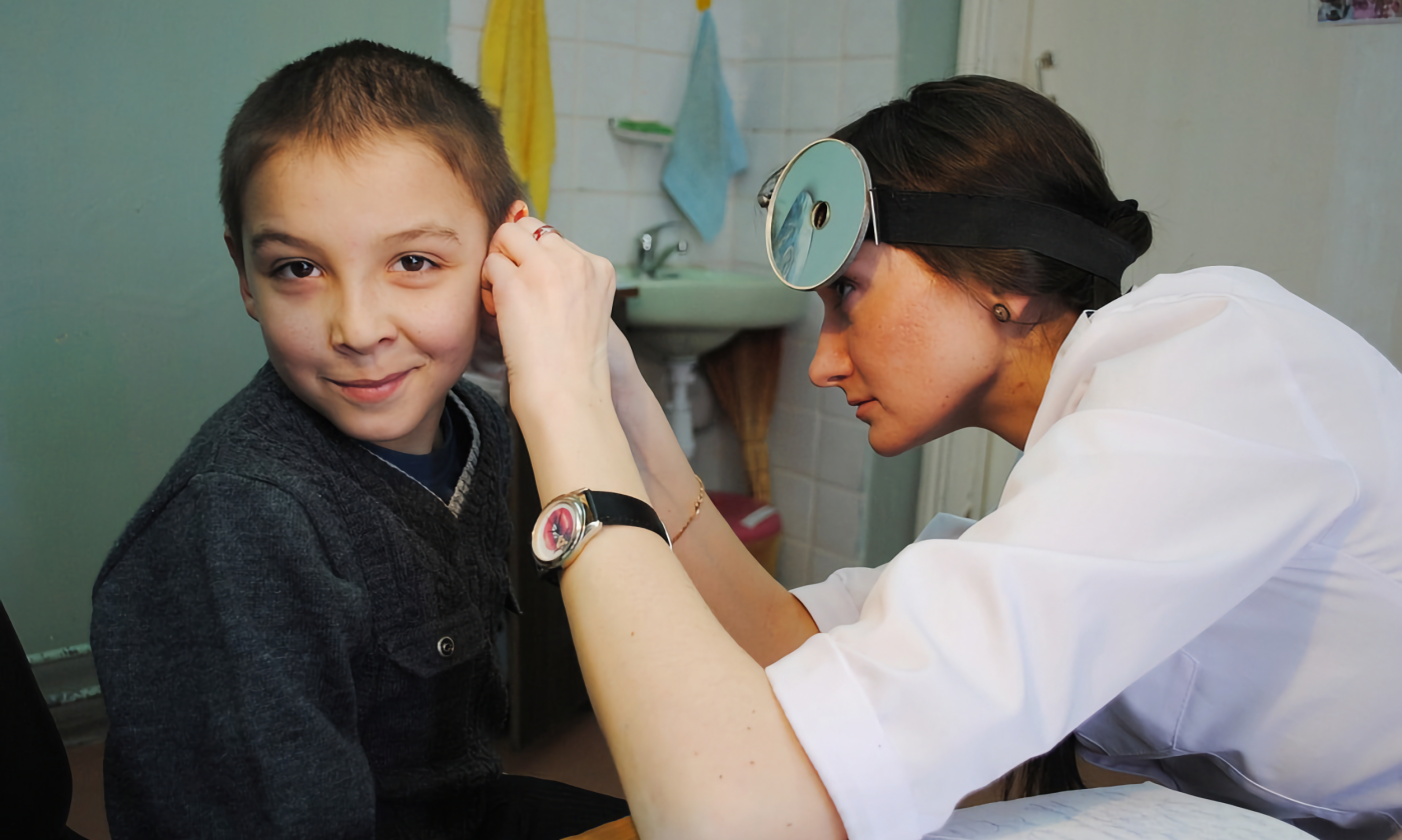 A young white boy getting his ear checked by a young white doctor. 