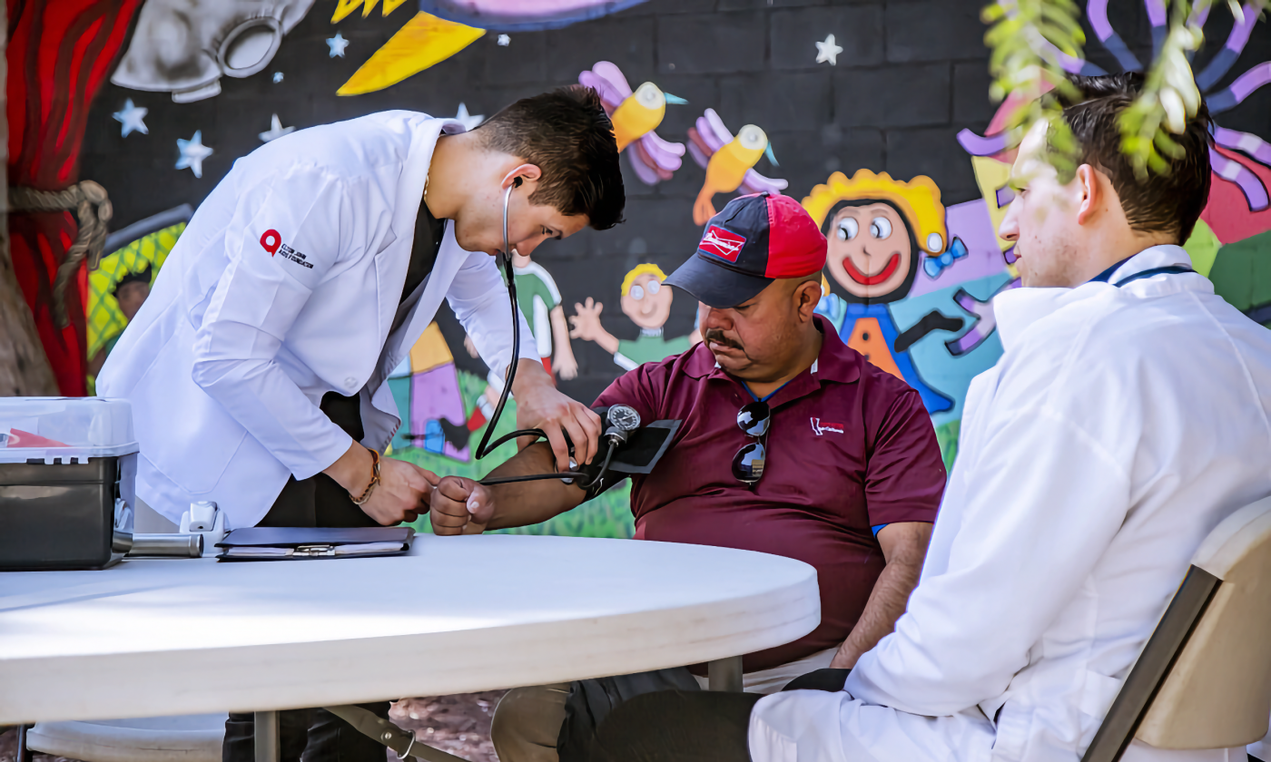 A full color image of two doctors caring for a patient (middle) both doctors are young men and their patient (wearing a hat) is an older man. 