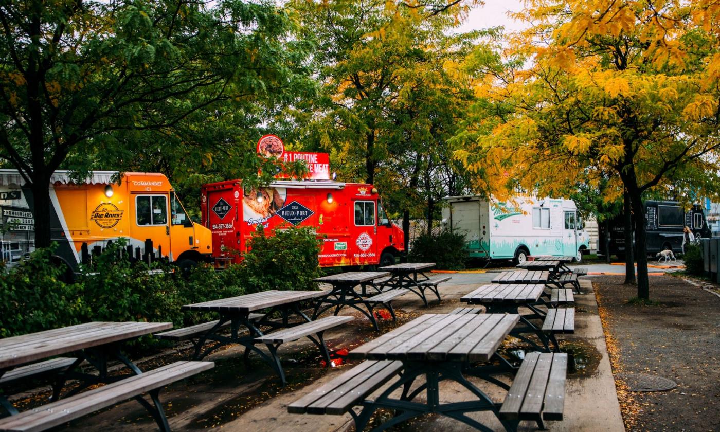 Three food trucks are positioned in front of a row of benches.