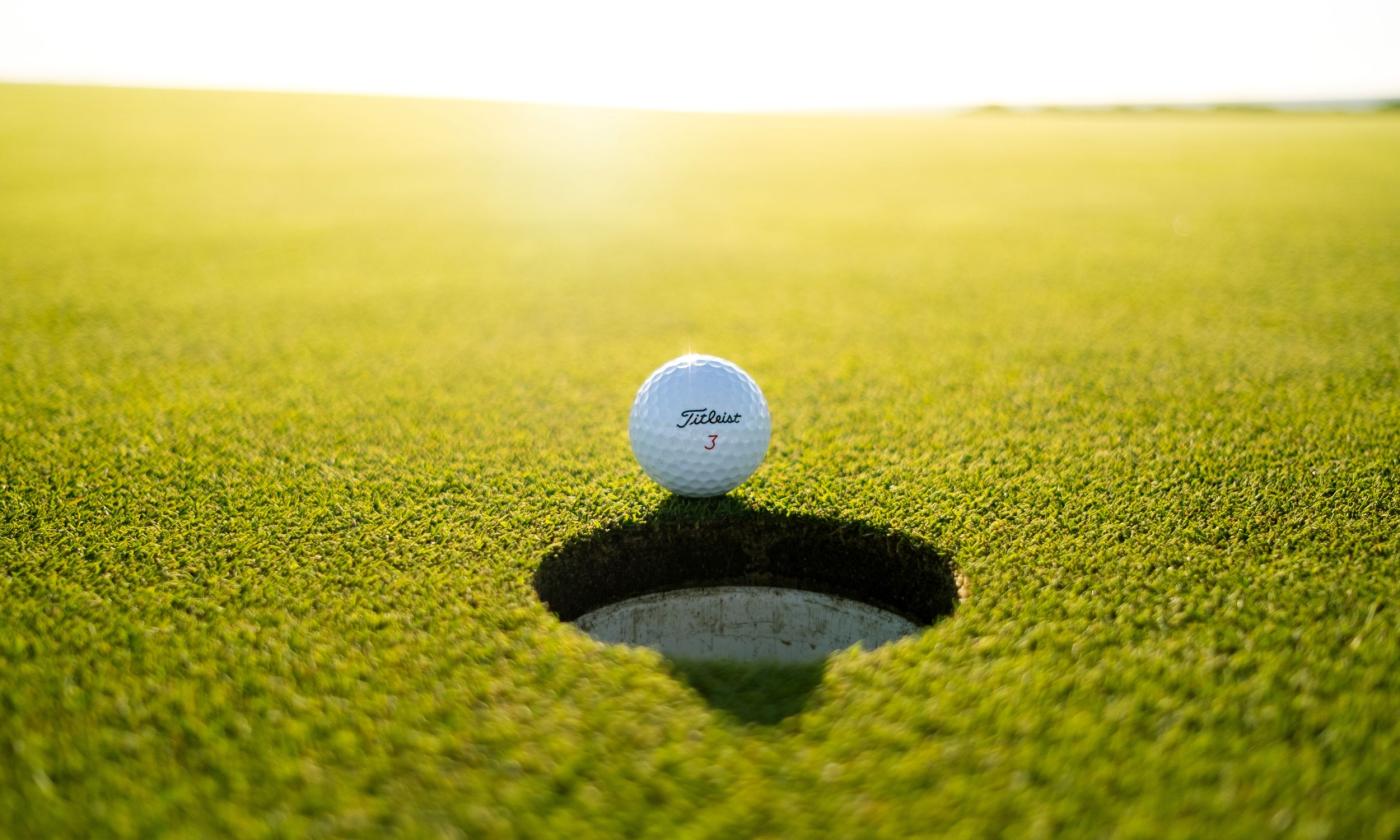A golf ball rolls next to a whole.