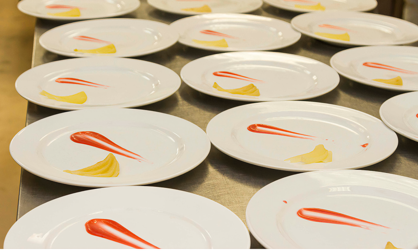 An array of plates on a table, decorated with bright sauces in preparation for a banquet