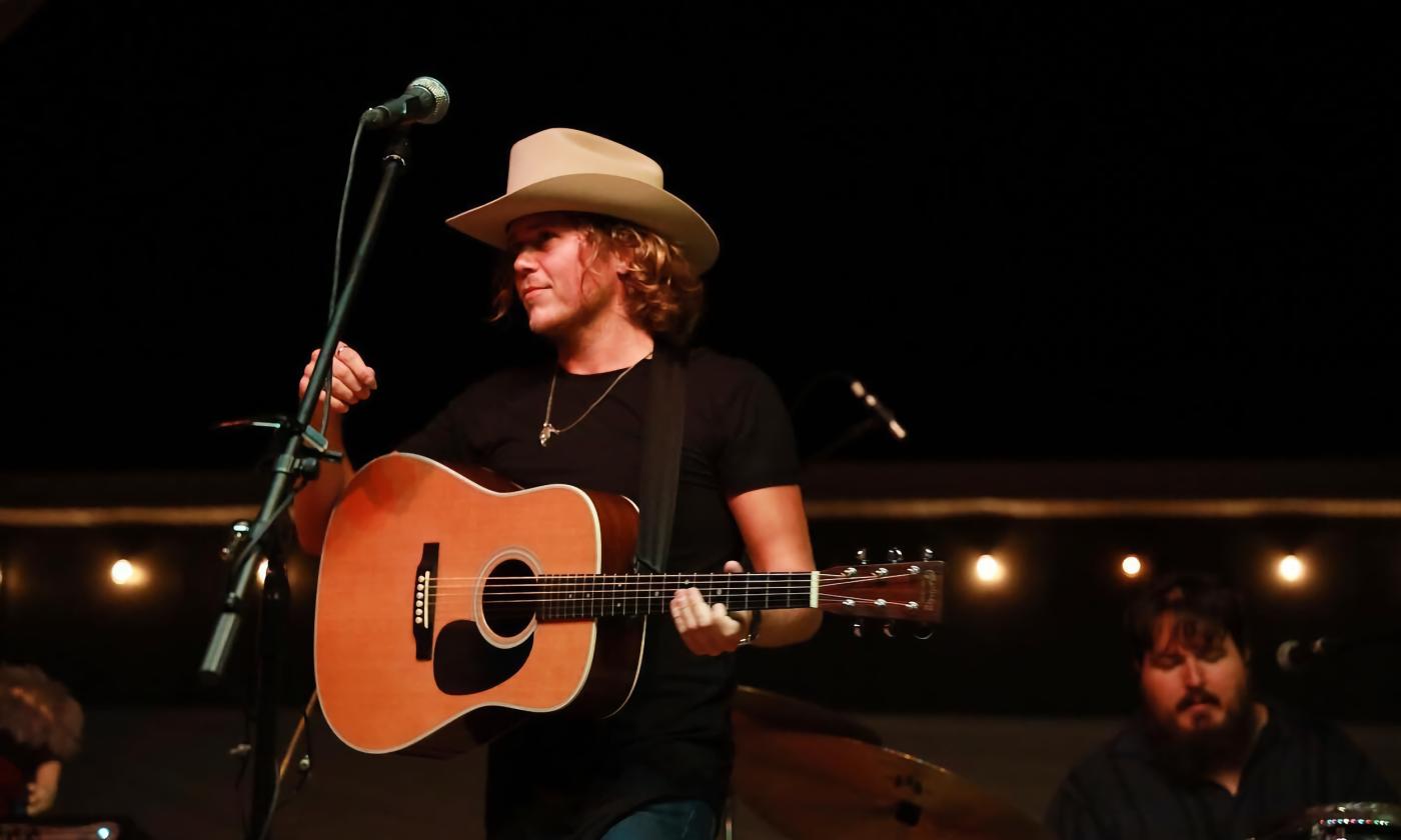 Christian Lopez holding a guitar and wearing a white hat on stage