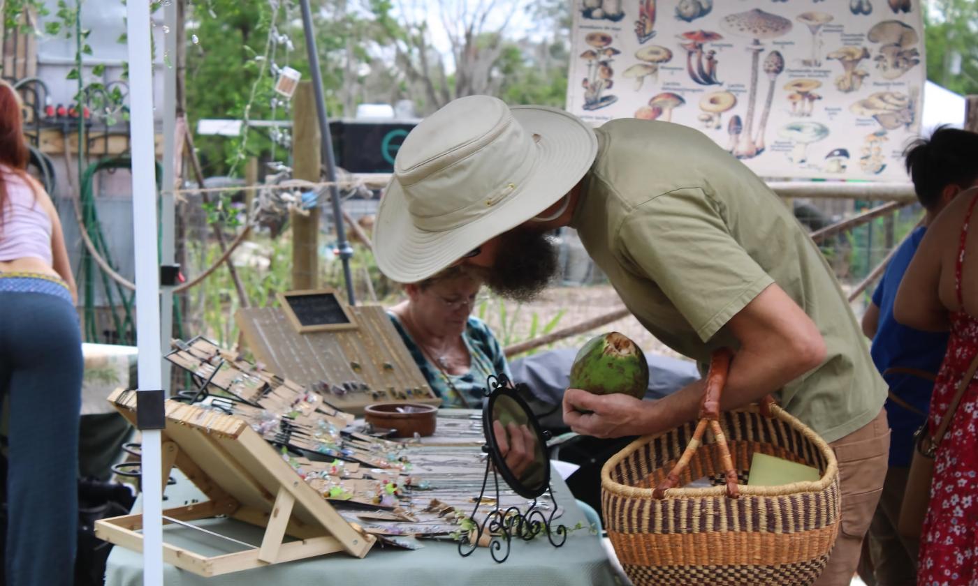 A bearded man holding a coconut peruses goods at the Earth Kinship Holisitc Gathering and Plant Swap