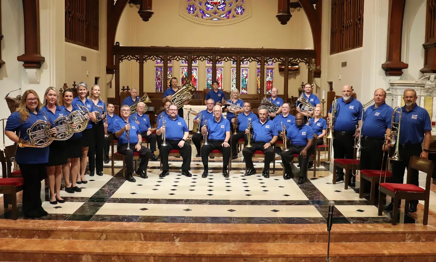 The members of Bold City Brass Band, in wearing blue shirts and black pants and arranged on stage.
