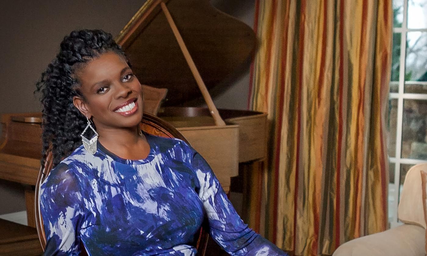 Vocalist Ann Marie McPhail, seated in a chair with an open grand piano behind her