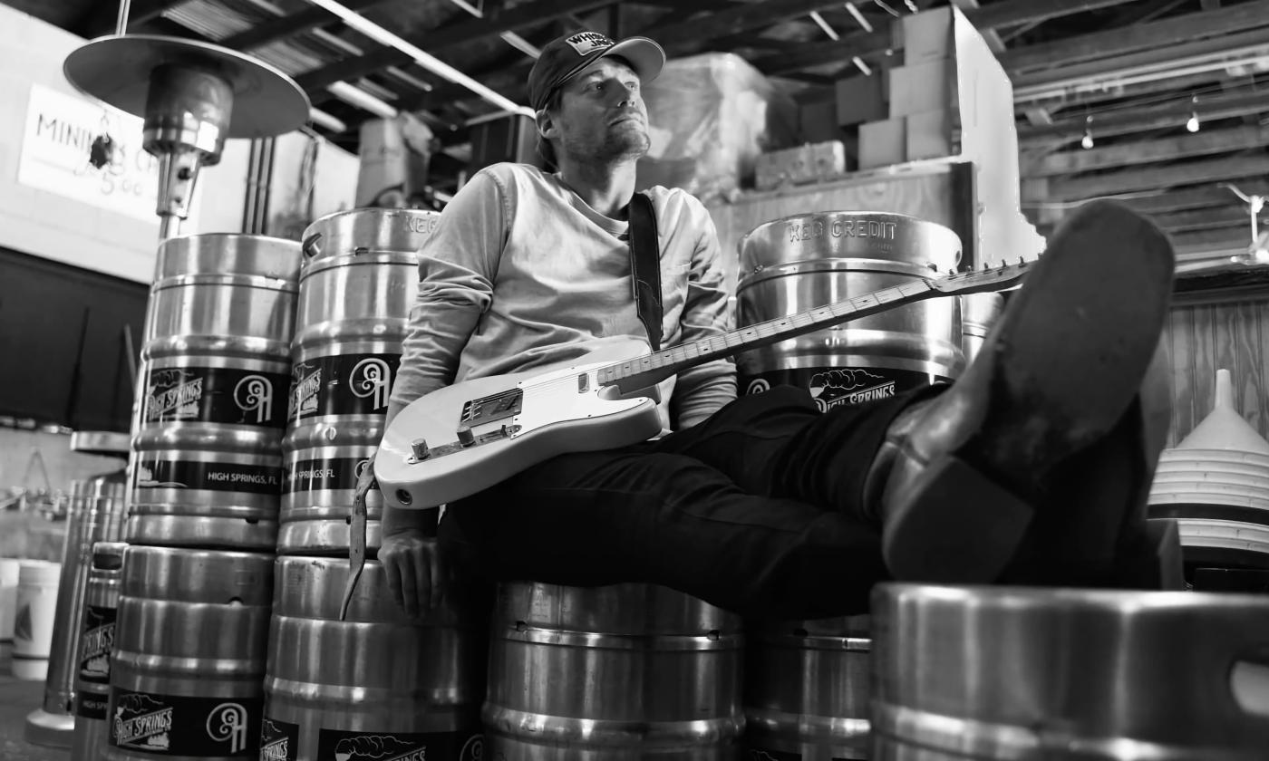 Upward shot of musician Justin Lee Partin reclining on a stack of beer kegs with an electric guitar in his lap