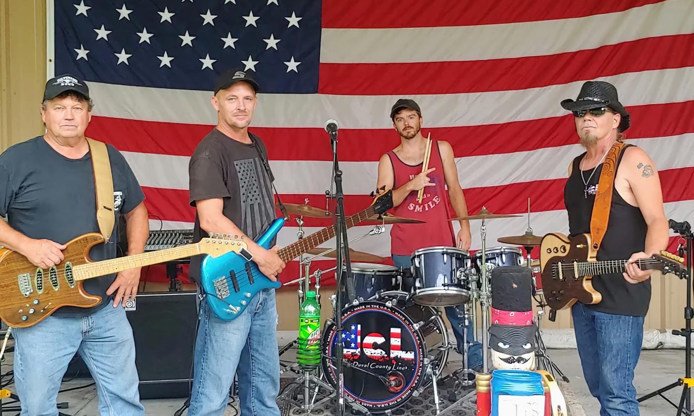 The four members of Duval County Line on stage with their instruments in front of the American Flag