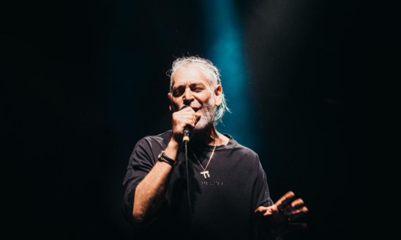  Iconic artist Matisyahu takes the stage and places the mic to his lips. His background is obscured. However, the floodlight from the stage illuminates his face and captures the moment when he belts out one of his songs