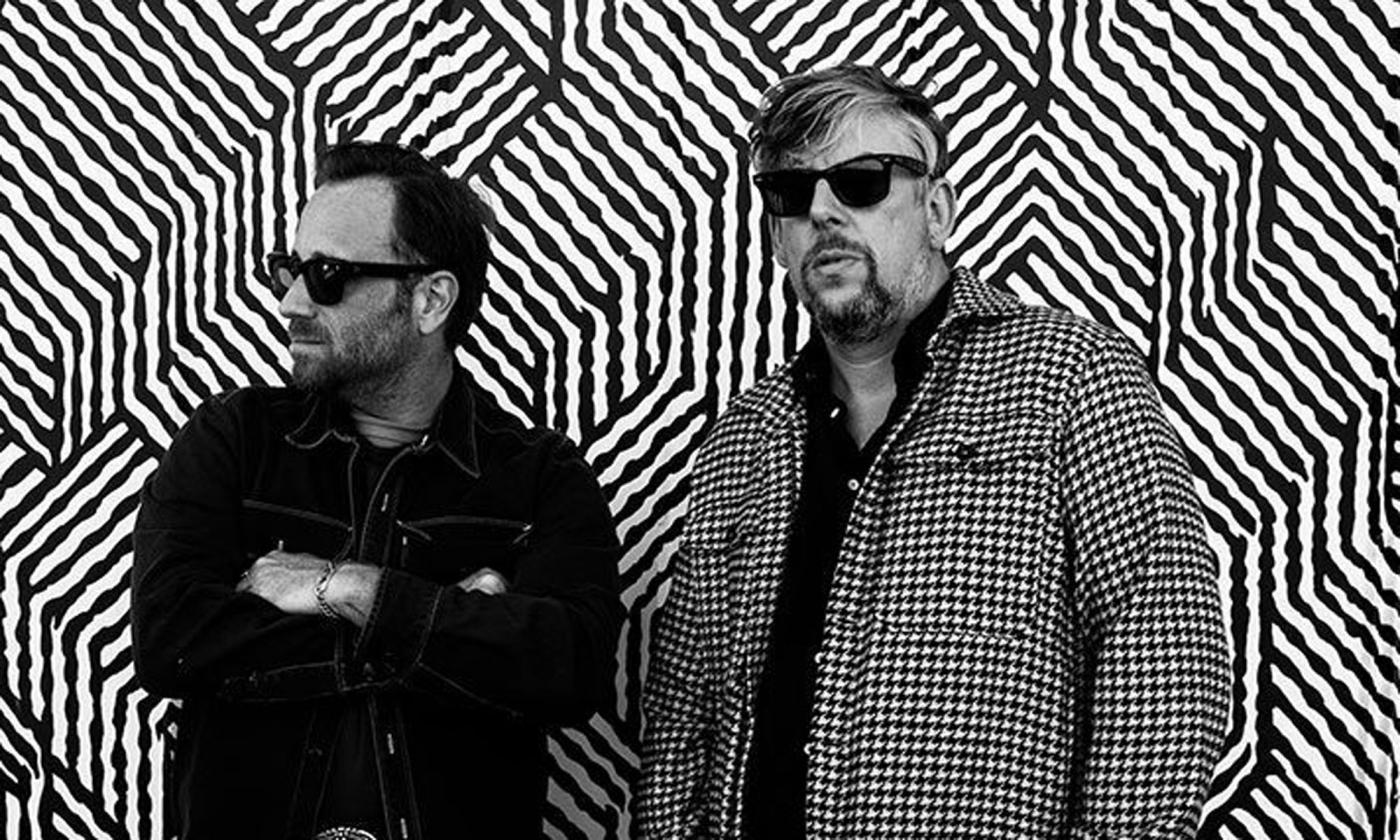 The Black Keys, Dan Auerbach and Pat Carney, wearing black and white and stading in front of a back and white geometric wall