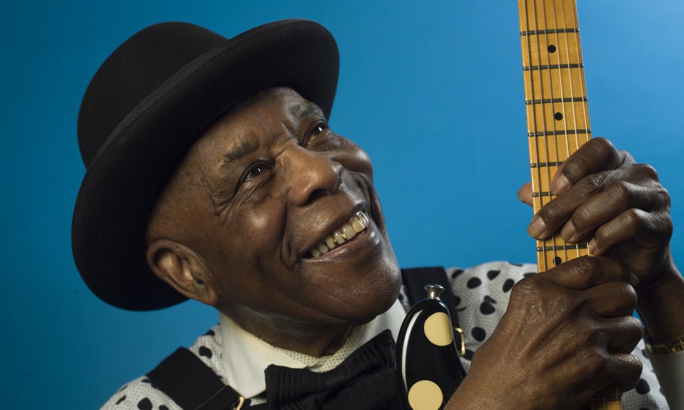 Buddy Guy grins and clutches his guitar. 