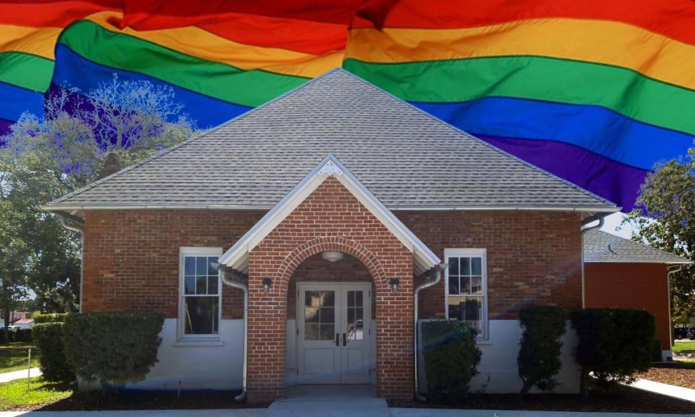 The simple brick entranceway to the Waterworks Building in St Augustine Florida. A row of rainbow pride flags fly in the sky behind the building