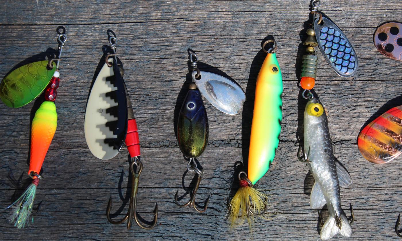 Colorful bait and fishing hooks are on a wooden board. 