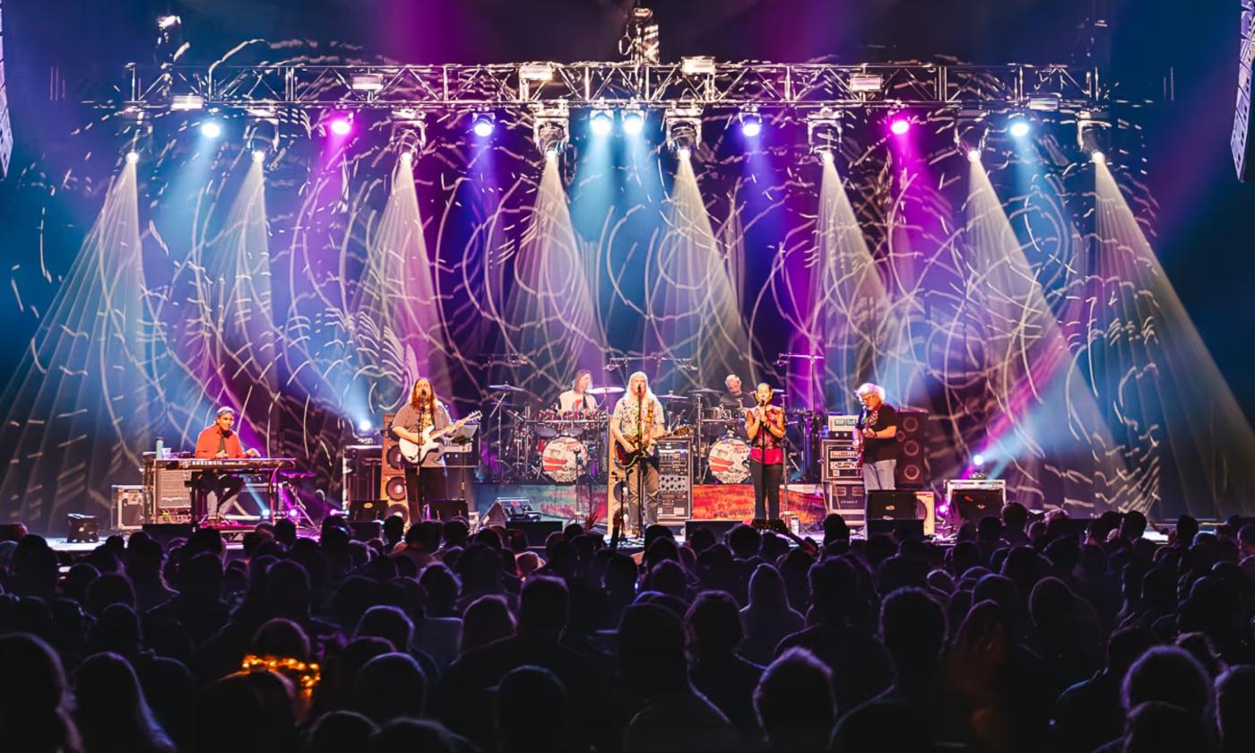 Band members of the Dark Orchestra performs live on a stage with colorful lights.