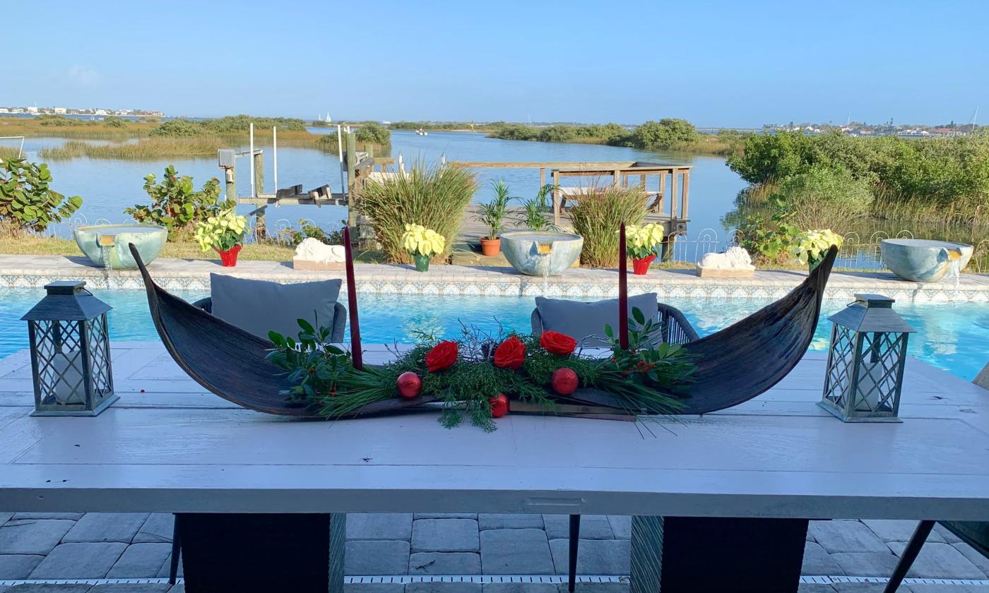 A gondola-shaped wooden tray, filled with red flowers and greenery, on a poolside table