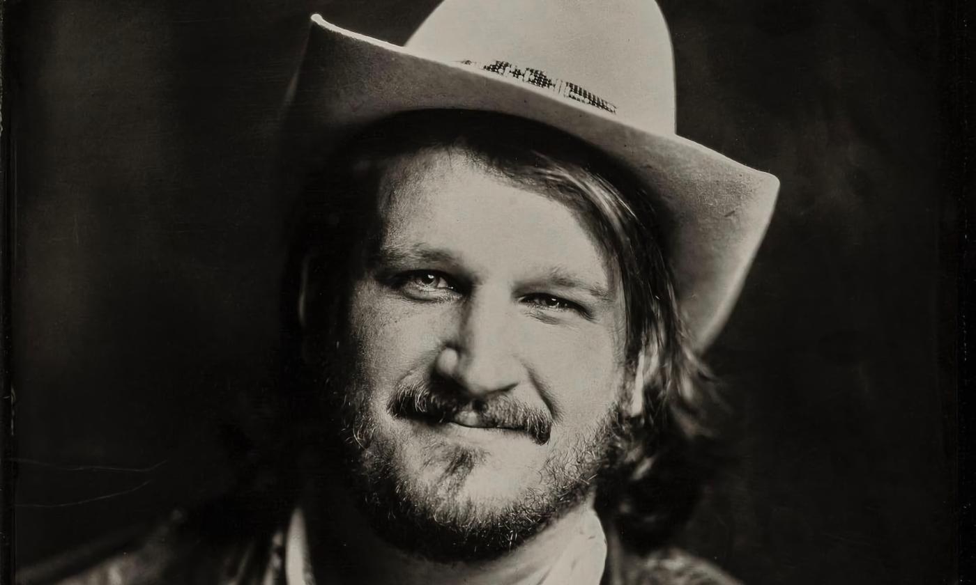 Willi Carlisle, musician, wearing a white cowboy hat against a black background
