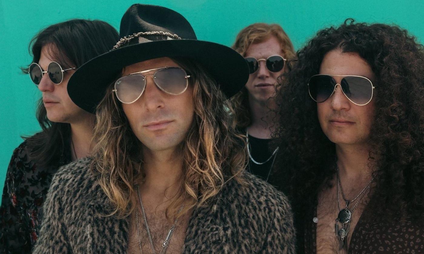 Members from the band Dirty Honey wear glasses and pose in front of a turquoise background.
