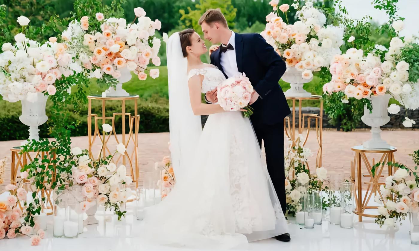 Bride and groom standing in front of large floral arrangements and decorative props