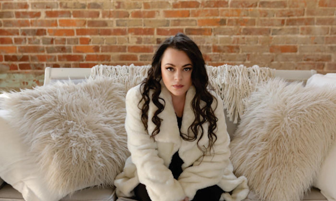 Mindy Smith sits on a plush white couch and smiles for the camera. 