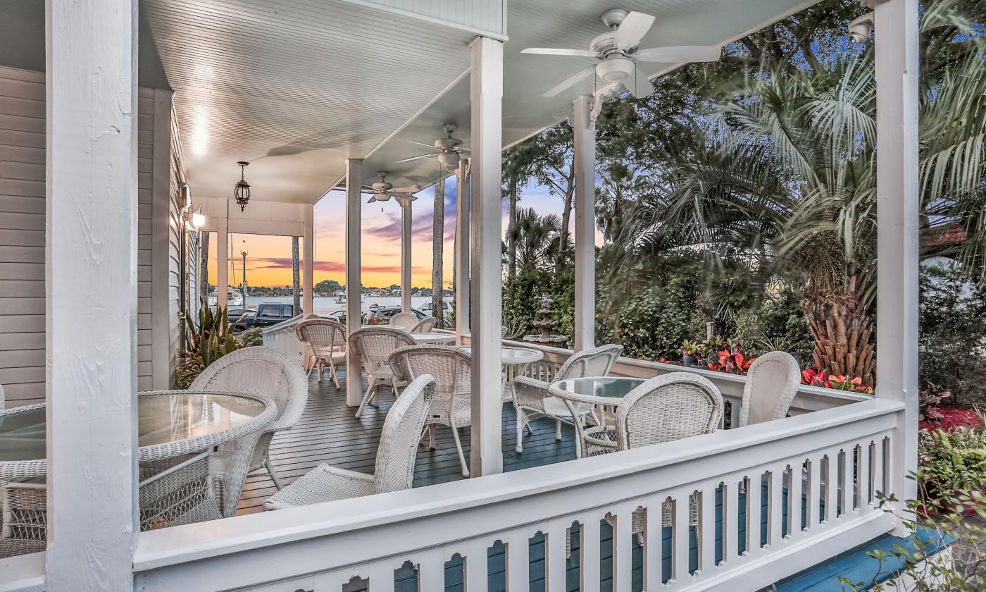 The charming porch at the Bayfront Wescott House, with wicker tables and chairs and a view of sunrise over the bayfront