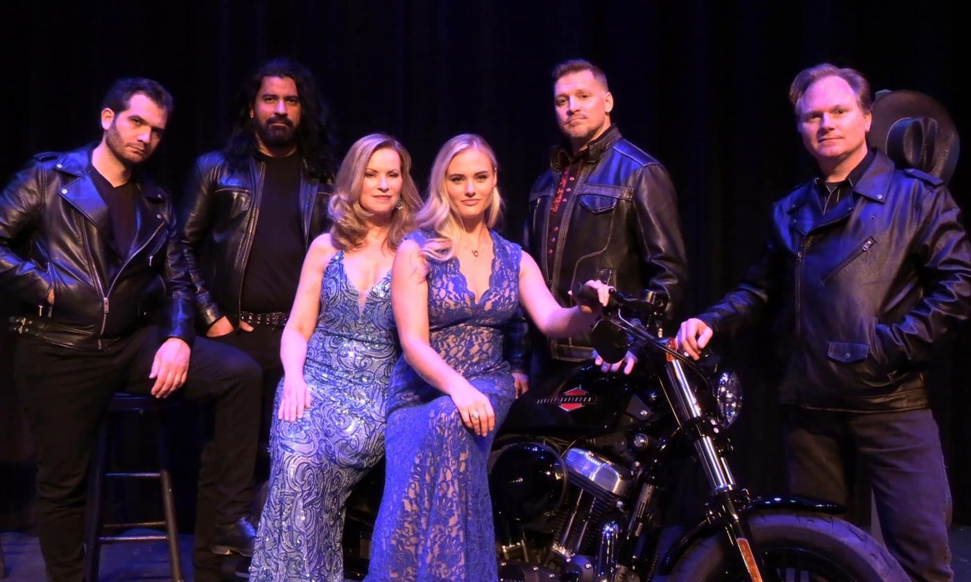 Four men in motorcycle leathers, and two women in gowns, members of Bad Boys of Opera, against a black background