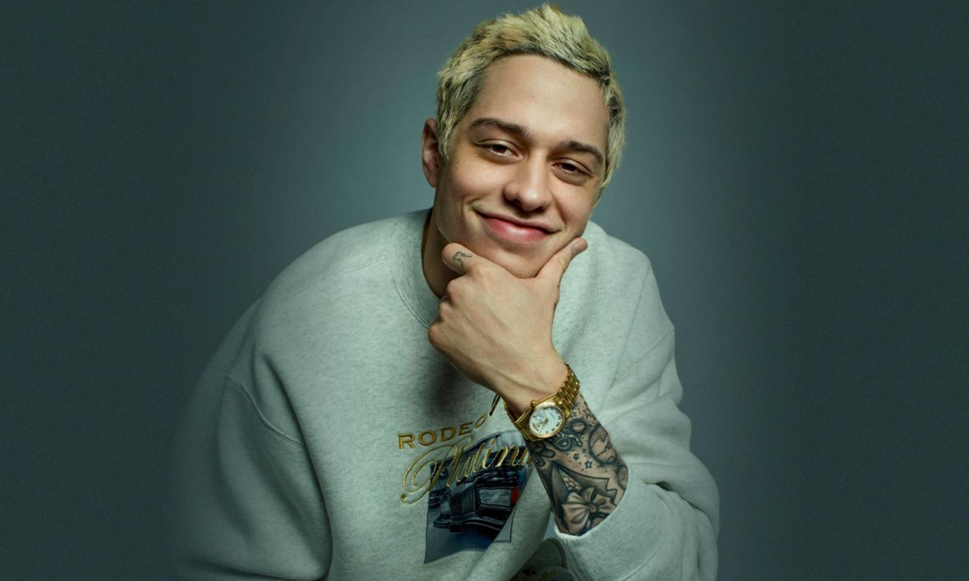 Comedian Pete Davidson smiles while clutching his chin.