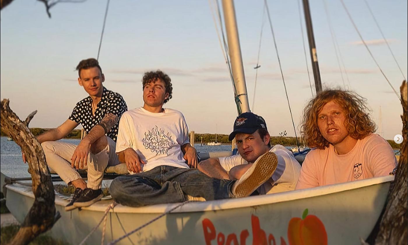 The four members of King Peach sitting in a small sailboat on land at sunset
