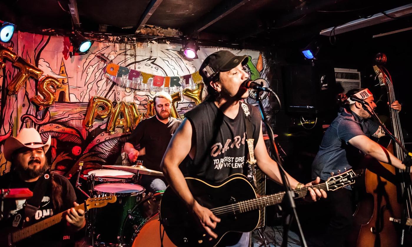 The four members of Mudtown performing on a stage with a colorful grafitti backdrop