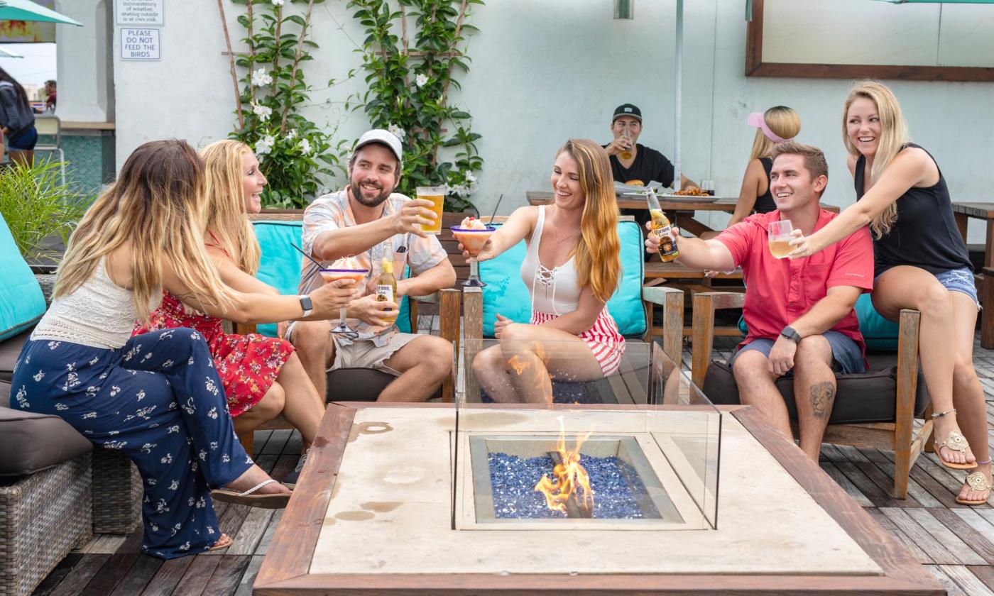 A party of guests sitting around the fire table and offering a toast at Salt Life Food Shack