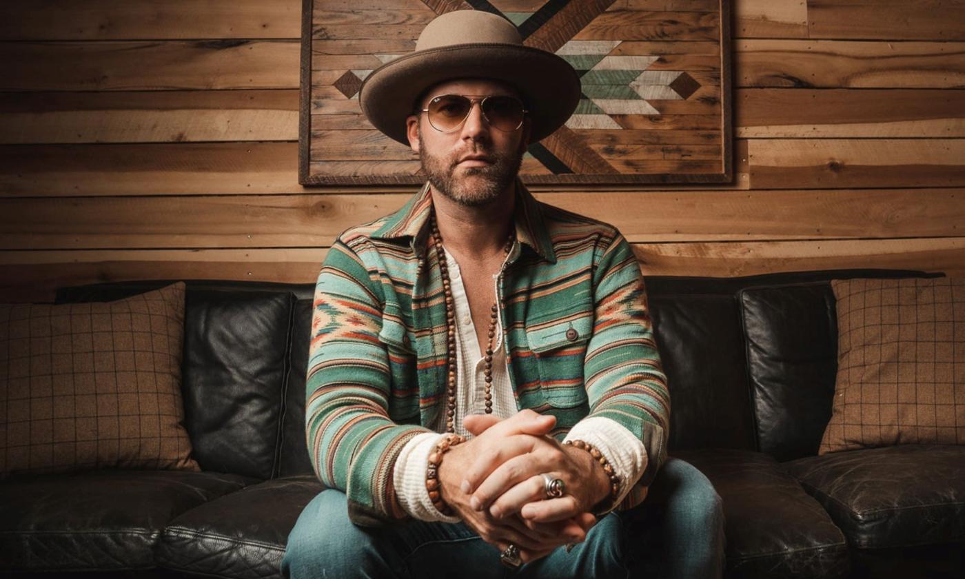 Drake White poses in front of a wooden wall with a Native American- inspired print on its surface. 