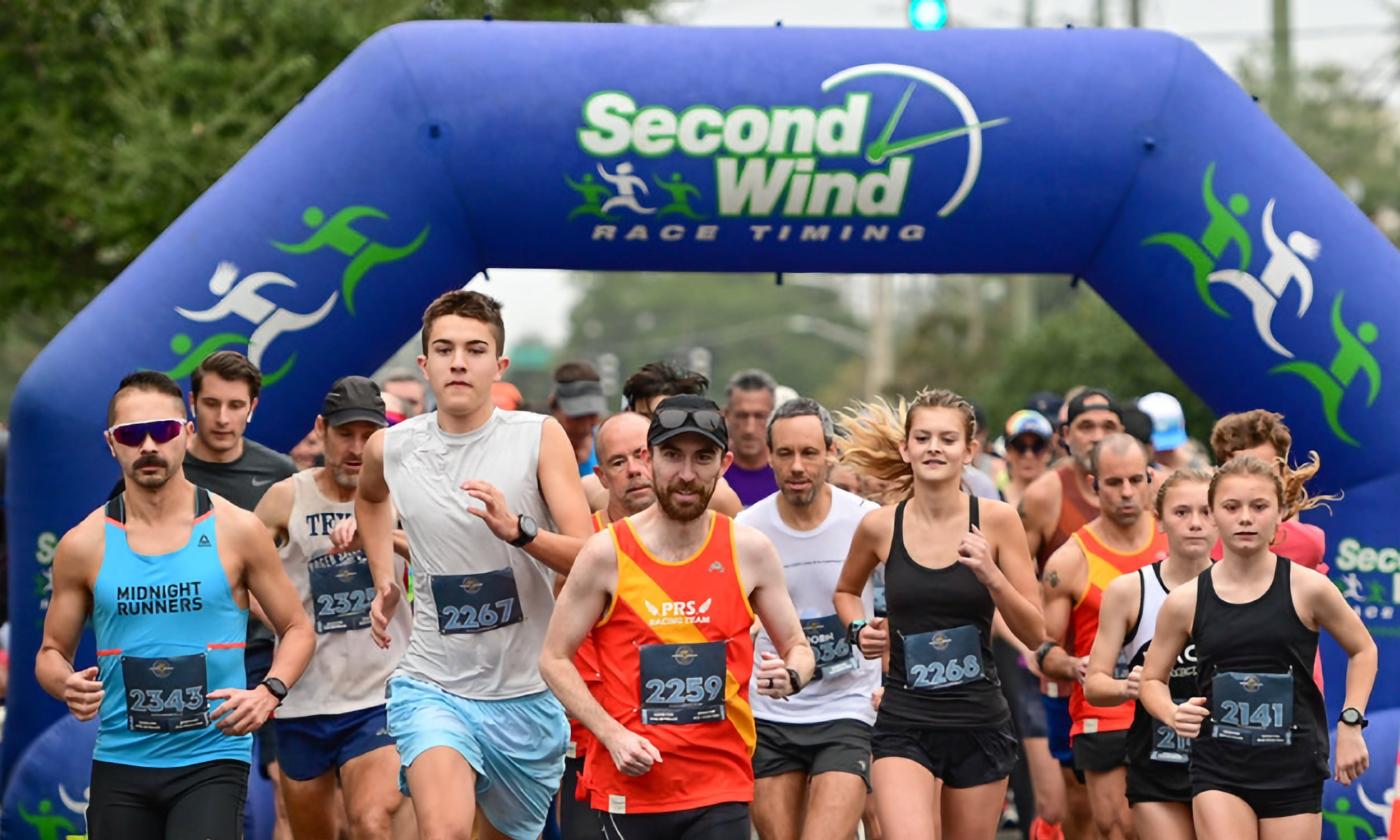 Runners at the starting line arch, with participants wearing numbered bibs and focused expressions