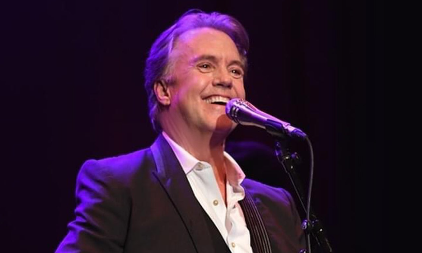 Shaun Cassidy smiles and sings with his lips positioned closely to the microphone.
